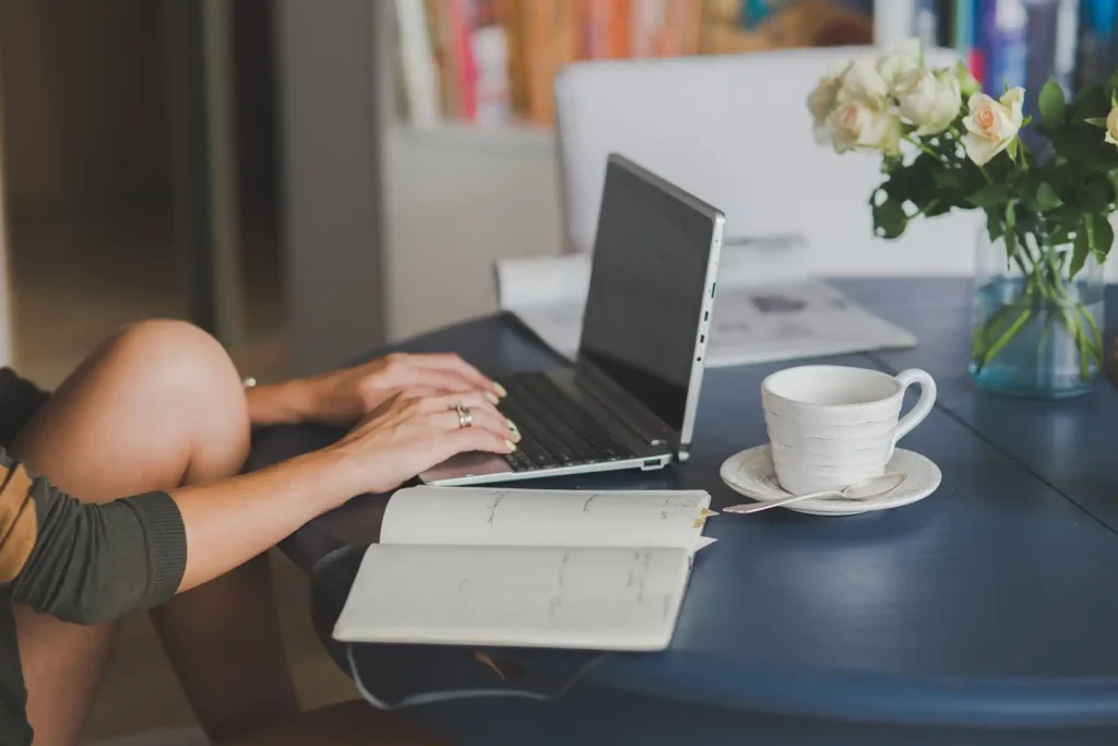 Egy vállalkozó ül a laptopjánál, mellette a jegyzetei és egy kávé az asztalon - a rólunk oldalát írja, próbál bizalmat építeni a honlapon